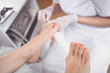 Pedikürcü özel bir aletle güzellik salonunda profesyonel tıbbi pedikür yapıyor. SPA salonunda ayak tedavisi. Ayak hastalıkları kliniği. Güzellik uzmanı kadın bacaklı beyaz eldivenler verdi.