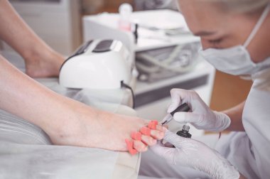 Pedikürcü, beyaz tırnak cilası sürüyor. Profesyonel tıbbi pedikür prosedürü. SPA salonunda ayak tedavisi. Ayak hastalıkları kliniği. Güzellik uzmanı beyaz eldivenlerle ellerini uzattı.