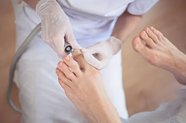 Hardware medical pedicure with nail file drill apparatus. Patient on pedicure treatment with pediatrician chiropodist. Foot peeling treatment at spa with a special device. Clinic of Podiatry Podology.