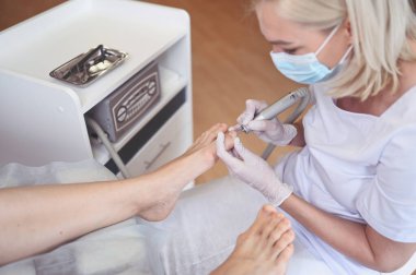 Tırnak törpüsü matkabıyla donanım tıbbi pedikür. Pediyatrist ayak hastalıkları uzmanıyla pedikür tedavisi gören hasta. Özel bir cihazla kaplıcada ayak soyma tedavisi. Podoloji Kliniği.