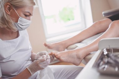 Profesyonel tıbbî pedikür prosedürü çift tırnak aletini kullanarak kapatılıyor. Hasta ayak hastalıkları uzmanını ziyaret ediyor. SPA salonunda ayak tedavisi. Ayak hastalıkları kliniği. Beyaz eldivenli pedikür elleri