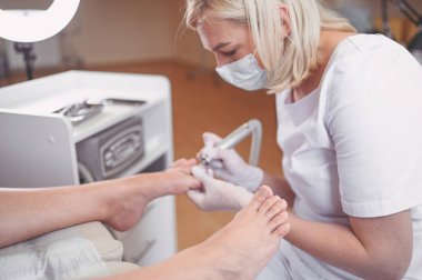Tırnak törpüsü matkabıyla donanım tıbbi pedikür. Pediyatrist ayak hastalıkları uzmanıyla pedikür tedavisi gören hasta. Özel bir cihazla kaplıcada ayak soyma tedavisi. Podoloji Kliniği.