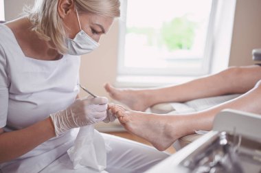 Profesyonel tıbbî pedikür prosedürü çift tırnak aletini kullanarak kapatılıyor. Hasta ayak hastalıkları uzmanını ziyaret ediyor. SPA salonunda ayak tedavisi. Ayak hastalıkları kliniği. Beyaz eldivenli pedikür elleri