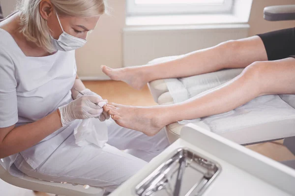 Profesyonel tıbbî pedikür prosedürü çift tırnak aletini kullanarak kapatılıyor. Hasta ayak hastalıkları uzmanını ziyaret ediyor. SPA salonunda ayak tedavisi. Ayak hastalıkları kliniği. Beyaz eldivenli pedikür elleri