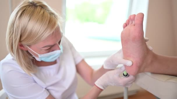 Podiatrist használ csiszoló berendezések és így eljárás lengyel lábpedikűr. Podology kozmetikus fehér kesztyű tisztítása bőr kliens lábak Callus és kukorica professzionális eszközzel. — Stock videók