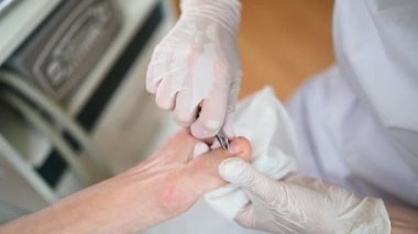 Tırnak makasıyla profesyonel tıbbi pedikür prosedürü. Hasta ayak hastalıkları uzmanını ziyaret ediyor. SPA salonunda ayak tedavisi. Ayak hastalıkları kliniği. Beyaz eldivenli pedikür elleri.