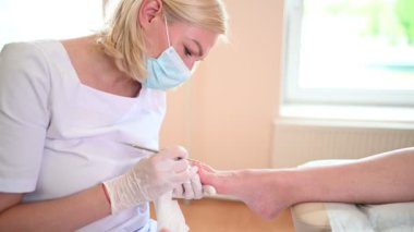 Profesyonel tıbbî pedikür prosedürü çift tırnak aletini kullanarak kapatılıyor. Hasta ayak hastalıkları uzmanını ziyaret ediyor. SPA salonunda ayak tedavisi. Ayak hastalıkları kliniği. Beyaz eldivenli pedikür elleri.