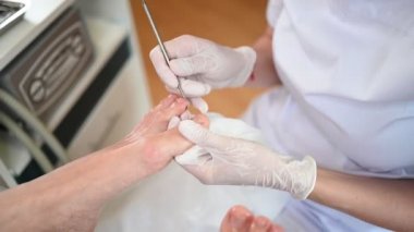 Profesyonel tıbbî pedikür prosedürü çift tırnak aletini kullanarak kapatılıyor. Hasta ayak hastalıkları uzmanını ziyaret ediyor. SPA salonunda ayak tedavisi. Ayak hastalıkları kliniği. Beyaz eldivenli pedikür elleri.