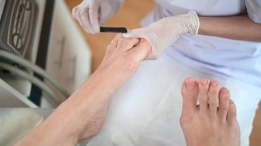 Pedikürcü güzellik salonunda tırnak törpüsü kullanarak profesyonel tıbbi pedikür yapıyor. SPA salonunda ayak tedavisi. Ayak hastalıkları kliniği. Güzellik uzmanı kadın bacaklı beyaz eldivenler verdi.