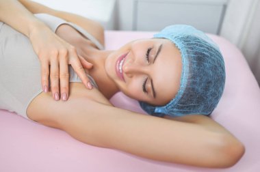 Güzellik salonunda lazer epilasyonu ve kozmetoloji. Saç çıkarma prosedürü. Balmumu tüy dökümü, kozmetoloji, spa, saç temizleme konsepti. Güzel, gülümseyen genç bir kadın koltuk altından tüyler aldırıyor.. 