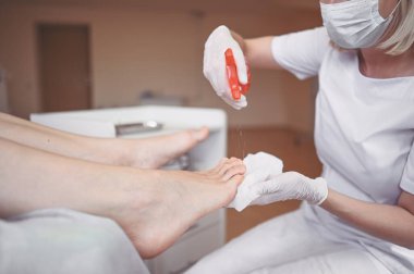 Pedikürcü özel bir aletle güzellik salonunda profesyonel tıbbi pedikür yapıyor. SPA salonunda ayak tedavisi. Ayak hastalıkları kliniği. Güzellik uzmanı kadın bacaklı beyaz eldivenler verdi.
