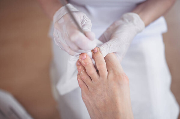 Professional medical pedicure procedure close up using double nail instrument. Patient visiting chiropodist podiatrist. Foot treatment in SPA salon. Podiatry clinic. Pedicurist hands in white gloves