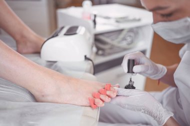 Pedikürcü, beyaz tırnak cilası sürüyor. Profesyonel tıbbi pedikür prosedürü. SPA salonunda ayak tedavisi. Ayak hastalıkları kliniği. Güzellik uzmanı beyaz eldivenlerle ellerini uzattı.