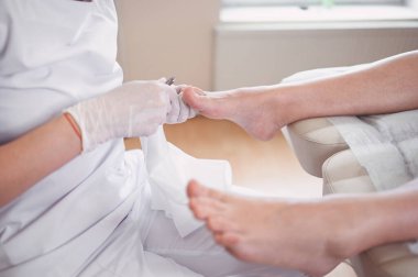Profesyonel tıbbi pedikür prosedürü tırnak makasıyla kapanır. Hasta ayak hastalıkları uzmanını ziyaret ediyor. SPA salonunda ayak tedavisi. Ayak hastalıkları kliniği. Beyaz eldivenli pedikür elleri
