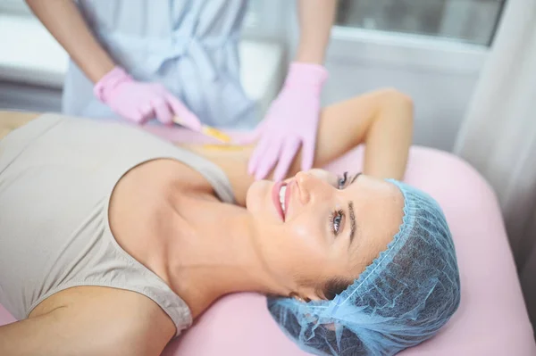 Waxing epilation and cosmetology in beauty salon. Hair removal procedure. Wax depilation, cosmetology, spa, hair removal concept. Beautiful smiling young woman getting hair removing on underarm.