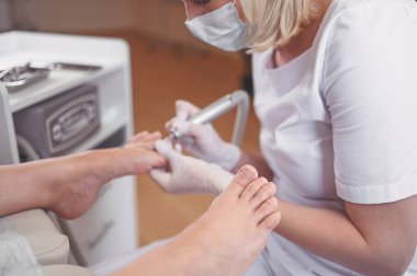 Tırnak törpüsü matkabıyla donanım tıbbi pedikür. Pediyatrist ayak hastalıkları uzmanıyla pedikür tedavisi gören hasta. Özel bir cihazla kaplıcada ayak soyma tedavisi. Podoloji Kliniği.
