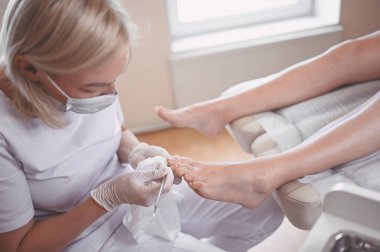 Profesyonel tıbbî pedikür prosedürü çift tırnak aletini kullanarak kapatılıyor. Hasta ayak hastalıkları uzmanını ziyaret ediyor. SPA salonunda ayak tedavisi. Ayak hastalıkları kliniği. Beyaz eldivenli pedikür elleri