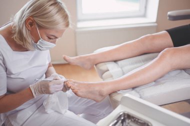 Profesyonel tıbbî pedikür prosedürü çift tırnak aletini kullanarak kapatılıyor. Hasta ayak hastalıkları uzmanını ziyaret ediyor. SPA salonunda ayak tedavisi. Ayak hastalıkları kliniği. Beyaz eldivenli pedikür elleri