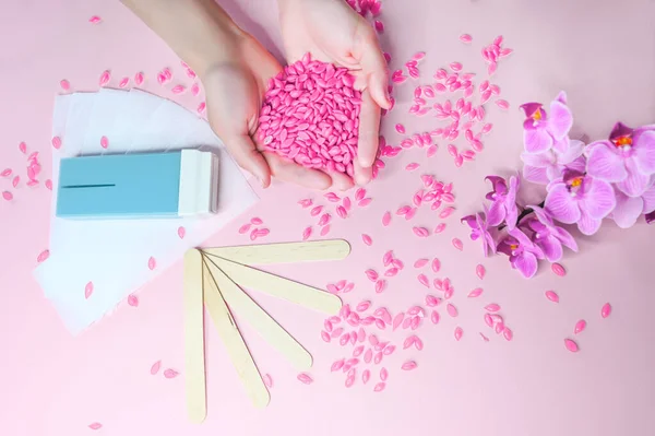 Set of depilation and beauty on pink background concept - sugar paste or hair removal waxing melted paste and stripes, orchid and female hands. Film Wax Granules or hot wax, cartridge, wooden spatula