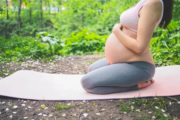 美丽的年轻孕妇在户外公园做瑜伽运动 坐在粉色瑜伽垫上休息 积极的未来母亲运动的生活方式 健康怀孕概念 — 图库照片