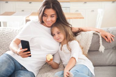 Çekici genç anne ve küçük kız akıllı telefon kullanarak online oyun oynuyorlar, görüntülü sohbet ediyorlar ya da film izliyorlar. Uzaktan eğitim. Karantina ile ilgili video konferansı veya sanal olay