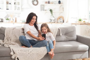 Çekici genç anne ve küçük kız akıllı telefon kullanarak online oyun oynuyorlar, görüntülü sohbet ediyorlar ya da film izliyorlar. Uzaktan eğitim. Karantina ile ilgili video konferansı veya sanal olay
