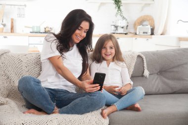 Çekici genç anne ve küçük kız akıllı telefon kullanarak online oyun oynuyorlar, görüntülü sohbet ediyorlar ya da film izliyorlar. Uzaktan eğitim. Karantina ile ilgili video konferansı veya sanal olay