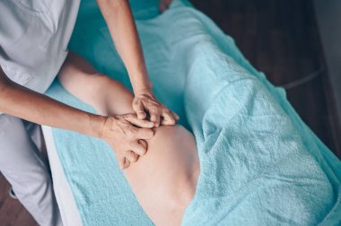 Masaj masasında uzanmış terapi masajından zevk alan tanınmayan genç bir kadın. Vücut bakımı, kilo verme konsepti. El masajı terapisti spa kliniğinde anti-selülit masaj yapıyor.
