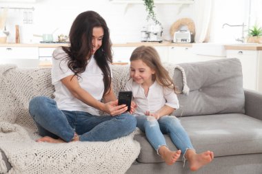 Çekici genç anne ve küçük kız akıllı telefon kullanarak online oyun oynuyorlar, görüntülü sohbet ediyorlar ya da film izliyorlar. Uzaktan eğitim. Karantina ile ilgili video konferansı veya sanal olay