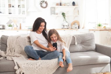 Çekici genç anne ve küçük kız akıllı telefon kullanarak online oyun oynuyorlar, görüntülü sohbet ediyorlar ya da film izliyorlar. Uzaktan eğitim. Karantina ile ilgili video konferansı veya sanal olay