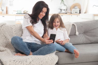 Çekici genç anne ve küçük kız akıllı telefon kullanarak online oyun oynuyorlar, görüntülü sohbet ediyorlar ya da film izliyorlar. Uzaktan eğitim. Karantina ile ilgili video konferansı veya sanal olay