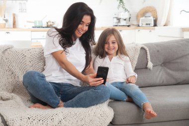 Çekici genç anne ve küçük kız akıllı telefon kullanarak online oyun oynuyorlar, görüntülü sohbet ediyorlar ya da film izliyorlar. Uzaktan eğitim. Karantina ile ilgili video konferansı veya sanal olay