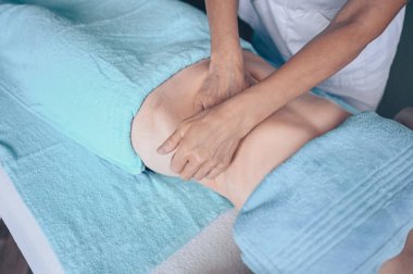 Masaj masasında uzanmış terapi masajından zevk alan tanınmayan genç bir kadın. Vücut bakımı, kilo verme konsepti. El masajı terapisti spa kliniğinde anti-selülit masaj yapıyor.