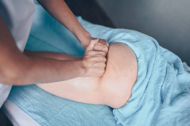 Masaj masasında uzanmış terapi masajından zevk alan tanınmayan genç bir kadın. Vücut bakımı, kilo verme konsepti. El masajı terapisti spa kliniğinde anti-selülit masaj yapıyor.
