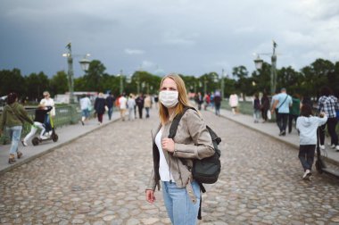 Covid 19 önleme için yüz koruyucu maske takmış genç sarışın bir kadın. Sırt çantalı beyaz öğrenci ya da gezgin turist. Corona virüsü konsepti.