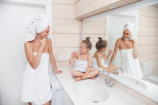 Happy loving family brushing teeth and spending time together. Mother and her daughter child girl kissing and hugging in white bathroom. Woman and girl with towels on their heads and bodies