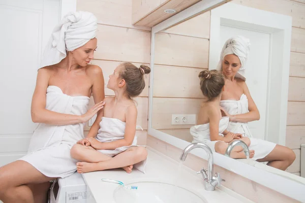 Happy loving family spending time together. Mother and her daughter child girl kissing and hugging in white bathroom. Woman and girl with towels on their heads and bodies