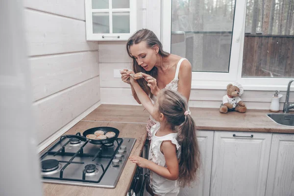 Happy loving family preparing cheesecakes for breakfast together. Beautiful young Mom and her cute child daughter girl cooking and having fun in the kitchen. Homemade healthy food with little helper