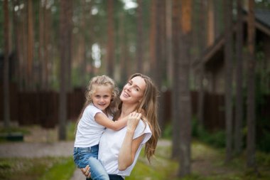 Mutlu gülümseyen annesi ve beyaz tişörtlü ve kot pantolonlu sevimli duygusal kızı kırsal alanda kucaklaşıp eğleniyorlar. Yazı ailemle geçiriyorum.