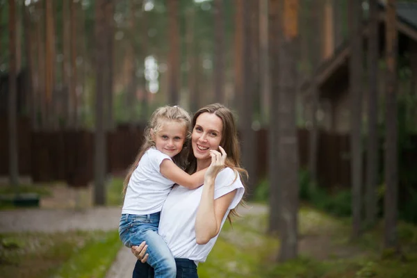 快乐的微笑着的母亲和她穿着白衬衫和牛仔牛仔的可爱的 情绪化的小女儿拥抱在一起 在乡间的大自然中享受着欢乐 与家人共度暑假 — 图库照片