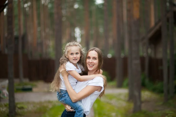 快乐的微笑着的母亲和她穿着白衬衫和牛仔牛仔的可爱的 情绪化的小女儿拥抱在一起 在乡间的大自然中享受着欢乐 与家人共度暑假 — 图库照片