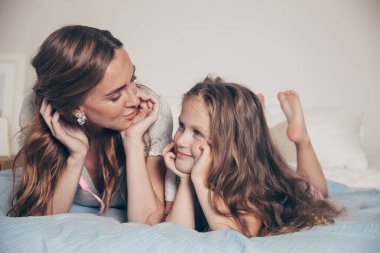 Mutlu ve sevgi dolu bir ailenin portresi yatak odasında uzanıp birlikte eğleniyor. Anne ve okul öncesi kızı pijamalı çocuk yatakta oynaşıp sarılıyorlar. Anneler günün kutlu olsun.