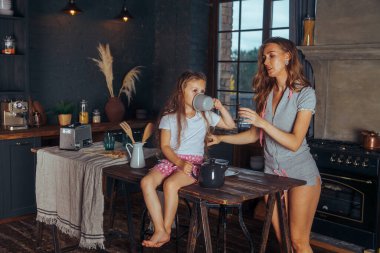 Mutlu bir aile yemeği hazırlıyor. Gülümseyen anne ve kız çocuğu mutfakta yemek pişiriyor ve eğleniyorlar. Ev yapımı sağlıklı yiyecekler. Evdeki karanlık bir mutfakta küçük bir yardımcı..