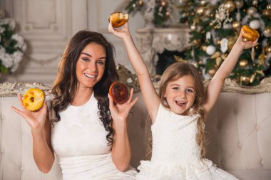 Güzel, genç ve güzel bir annesi olan, süslenmiş bir Noel ağacının arka planında eğlenen ve donut yiyen küçük, tatlı bir kız. Mutlu bir aile yeni yıl şenlik gecesinde. 