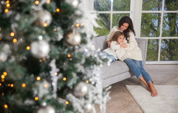 Yeni yıl arifesinde mutlu bir aile. Genç, güzel bir anne ve beyaz, rahat kazaklar içinde, pencerenin yanındaki kanepede sarılan ve Noel ağacını süsleyen tatlı bir kız. Şenlikli ev klasiği iç mimarisi.