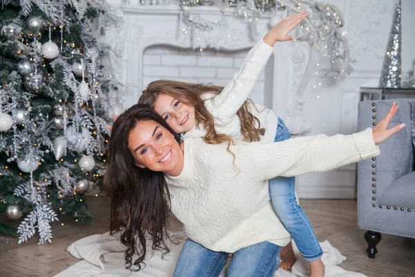 Yeni yıl arifesinde mutlu bir aile. Süslü süveter ve battaniye içinde güzel bir anne ve tatlı bir kız çocuğu süslü bir Noel ağacının altında eğleniyor ve sarılıyorlar. Şenlikli ev klasiği iç mimarisi.