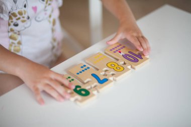 Anaokulunda masa başında otururken okul için hazırlanan, ahşap matematiksel çok renkli figürlerle eğitim oyunları oynayan anaokulu çocuğu elleri. Okul konseptine dönelim.