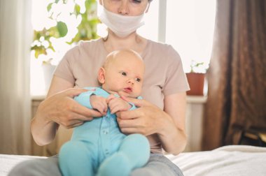 Koruyucu yüz maskesi takmış güzel bir anne kucağında yeni doğmuş oğlunu virüslerden ve enfeksiyonlardan koruyor. Coronavirus covid-19 önleme. Ev karantinası. Evde mutlu bir aile.