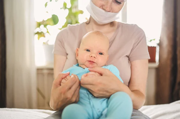 Прекрасна мати в захисній масці, тримаючи свого милого новонародженого сина, захищає його від вірусів та інфекцій. Coronavirus covid-19 Дім карантину. Щаслива родина вдома.. — стокове фото