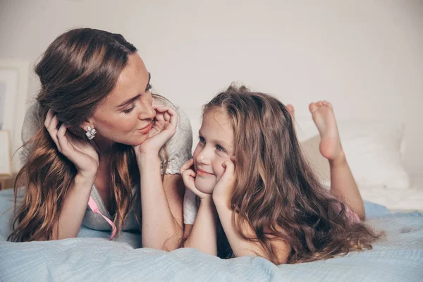 Mutlu ve sevgi dolu bir ailenin portresi yatak odasında uzanıp birlikte eğleniyor. Anne ve okul öncesi kızı pijamalı çocuk yatakta oynaşıp sarılıyorlar. Anneler günün kutlu olsun.